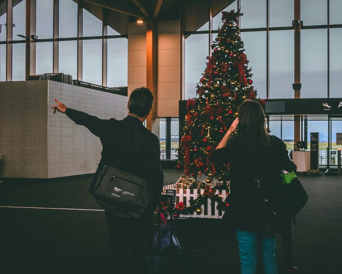 Couple at airport in front of a Christmas tree.